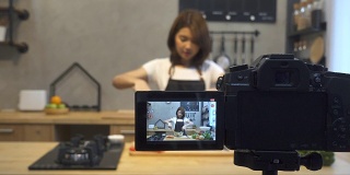 年轻的亚洲女人在厨房里给摄像机录像。微笑的亚洲女人工作的食物博主概念与水果和蔬菜在厨房。
