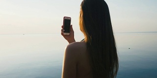 漂亮的年轻女子与她的智能手机在日落海滩附近的海边度假。慢动作