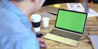 4k分辨率亚洲商人穿着休闲服装在咖啡店的绿色屏幕上使用电脑笔记本电脑，模仿商业广告的概念