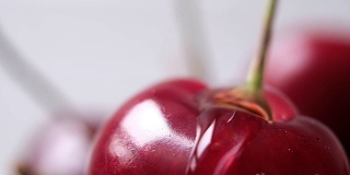 一颗成熟的樱桃在白色的背景上淌下一滴水。近距离微距镜头，慢动作。