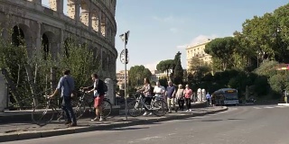 年轻美丽的女子游客在罗马市中心斗牛场过马路在阳光明媚的一天慢镜头汽车稳定摄影机