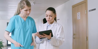 在医院里，忙碌的医生在走廊里一边聊天一边使用平板电脑。新型现代化、功能齐全的医疗设施。