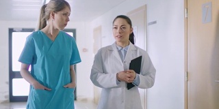 护士和医生走过医院走廊，交谈，讨论现代医疗程序。专业人士拯救生命。