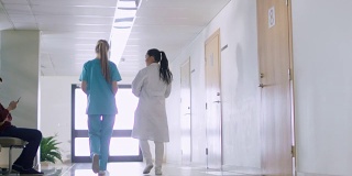 低角度拍摄护士和医生走过医院走廊，交谈，讨论现代医疗程序。专业人士拯救生命。