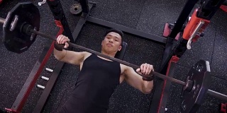 年轻的亚洲肌肉男子躺着和锻炼杠铃卧推在健身房，生活方式运动和健美的概念