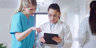 在医院里，忙碌的医生在走廊里一边聊天一边使用平板电脑。新型现代化、功能齐全的医疗设施。