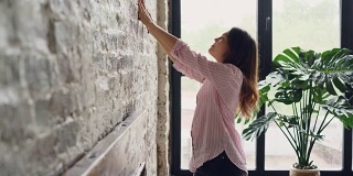 有创意的女人正在装饰她的阁楼风格的公寓，在砖墙上选择美丽的图片和标记点用铅笔。创意和室内概念。