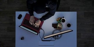 一个穿着黑帽衫的年轻人在晚上侵入笔记本电脑，坐在桌子后面拿着笔记本电脑和显示器，上图