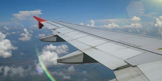 4 k。乘飞机旅行。通过飞机窗口的鸟瞰图与光线从len耀斑。机翼飞机和美丽的白云在蓝天为背景