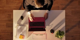 一个戴眼镜穿西装的年轻人走进来，坐在桌子后面，打开笔记本电脑打字