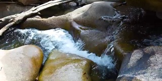 小溪清澈的水在湍急的河流从山上瀑布近距离。水流在岩石密布的河里迅速流动。从丛林中的瀑布倾泻到山河中的石头上的水流
