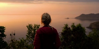 在日落的慢镜头中，科西嘉岛海岸线上的悬崖上的女人和偏远的海滩