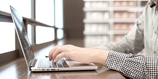 年轻的亚洲商人在工作空间使用笔记本电脑，木桌上放着智能手机和笔记本。男性用手在笔记本电脑键盘上打字。数字时代概念中的自由职业生活方式。