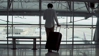 4 k。男性年轻乘客使用智能手机带着行李箱行走，坐在机场候机楼出发区的长凳上。正在出差的亚洲商人。现代旅游生活理念视频素材模板下载