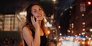 在美国纽约，年轻快乐的女人晚上拿着包站在市中心的车流中打电话