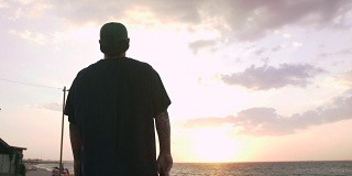 在日出时，一个年轻人带着滑板望着大海