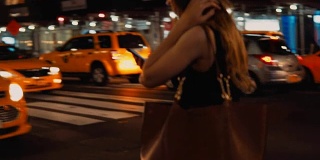 在纽约市中心，一个年轻女子在晚上使用智能手机过马路的特写