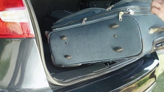 特写:一个面目全非的男人把旅行袋放在宽敞的汽车后备箱里。视频素材模板下载
