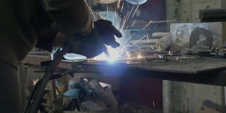 近距离的一个职业妇女铁匠使用焊机修理的东西充满了她的工业车间与火花