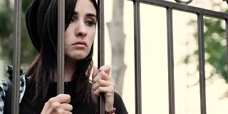 一个悲伤绝望的女孩透过栅栏望着，叹息着