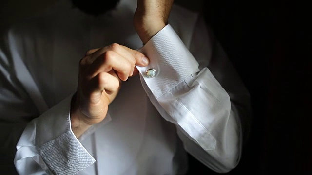 穿白衬衫的人调整袖子上的袖扣