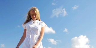 微笑的年轻女子在白色的裙子在蓝色的天空