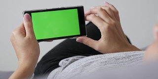 女性放松在床上与绿色屏幕显示智能手机平移