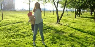 年轻的母亲和她的孩子在公园里转圈。快乐的家庭在夕阳下玩耍