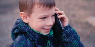 男孩在公园里用手机说话，笑着说。正面，特写。