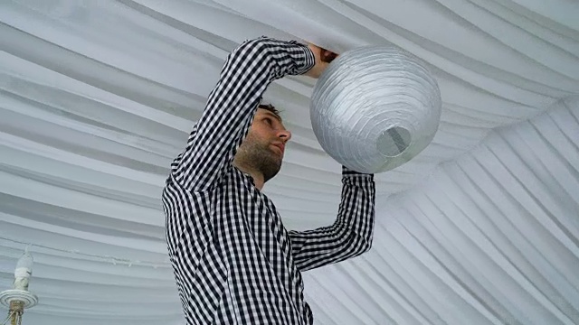 男人在天花板上挂着五颜六色的白粉灰纸灯笼。