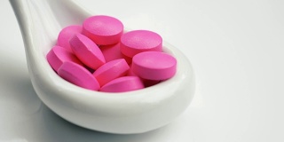 粉红色的药掉到白色的勺子里。孤立在白色背景上。勺子上有粉色药丸。