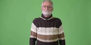 英俊的年长胡须男子穿着暖和的衣服，以绿色为背景