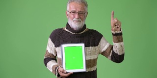Handsome senior bearded man wearing warm clothing against green background