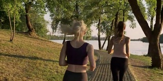 两个年轻漂亮的女跑步者在公园对面的桥上慢跑，减肥，健身模特跑步，从后面看