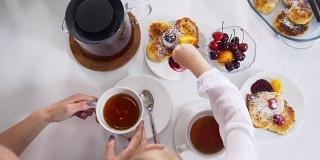 妈妈和她的小女儿一边喝茶，一边吃自制的糖果和水果