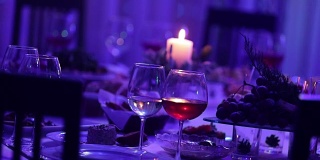 餐厅的宴会桌上放着玻璃杯和一支蜡烛，宴会桌上放着一杯红白葡萄酒，背景上放着一支燃烧的蜡烛，桌子上挂着一支装饰性的蜡烛