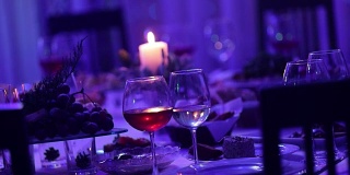 餐厅的宴会桌上放着玻璃杯和一支蜡烛，宴会桌上放着一杯红白葡萄酒，背景上放着一支燃烧的蜡烛，桌子上挂着一支装饰性的蜡烛