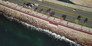 在岩石海岸旁边的高速公路上，空中的镜头跟随着汽车。股票。海岸线沿线及高速公路鸟瞰图