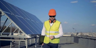 有太阳能电池板的屋顶，一个工程师在上面举着安全帽