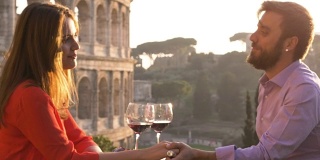 夕阳西下，浪漫优雅的情侣坐在罗马斗牛场前的餐厅桌前，手握红酒谈心