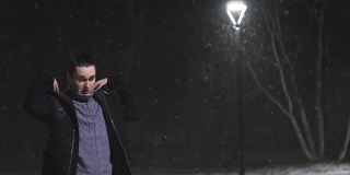 路灯下的那个人。在灯光的映衬下，正在下雪。慢动作，每秒180帧。雪花很漂亮。那个男人穿着一件凉爽的黑外套。