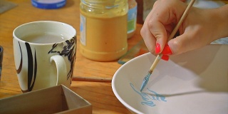 年轻的艺术家，在陶艺工坊里，用画笔在泥板上作画。小型企业