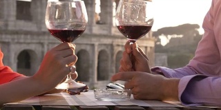 日落时分，一对浪漫的情侣坐在罗马斗牛场前的餐厅桌前，喝着红酒敬酒