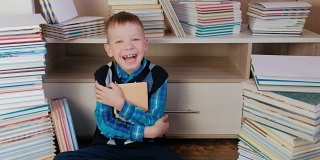 7岁的小男孩抱着书，对着镜头微笑，坐在书中。特写镜头。