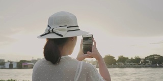 复古风格的泰国女性后视图是用智能手机拍照，在日落之前拍摄河流的景色