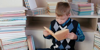 一个七岁的小男孩从书堆里拿出书，坐在书堆里看书。