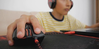 青少年使用笔记本电脑。青少年耳机使用有线鼠标垫。特写手点击和滚动电脑游戏黑红鼠标。
