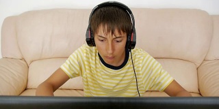 青少年使用笔记本电脑。沉迷于视频游戏的青少年用耳机粘在笔记本屏幕上按键盘。