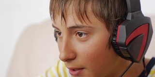 青少年使用笔记本电脑。特写的十几岁的男孩与耳机语音聊天，而玩在线游戏。