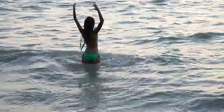 穿着比基尼的女人在海滩上玩水后视图，快乐的女性游客在暑假